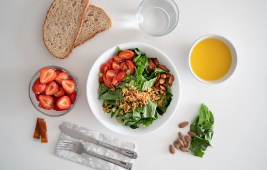 Top view of a healthy salad and fresh ingredients with bread and juice on a white surface.